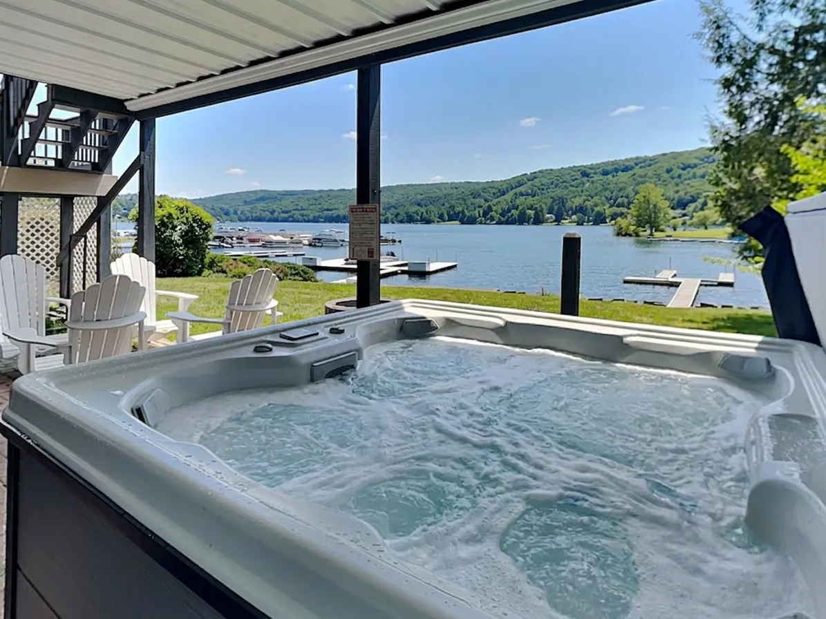 A bubbling hot tub sits on a covered lakeside deck.
