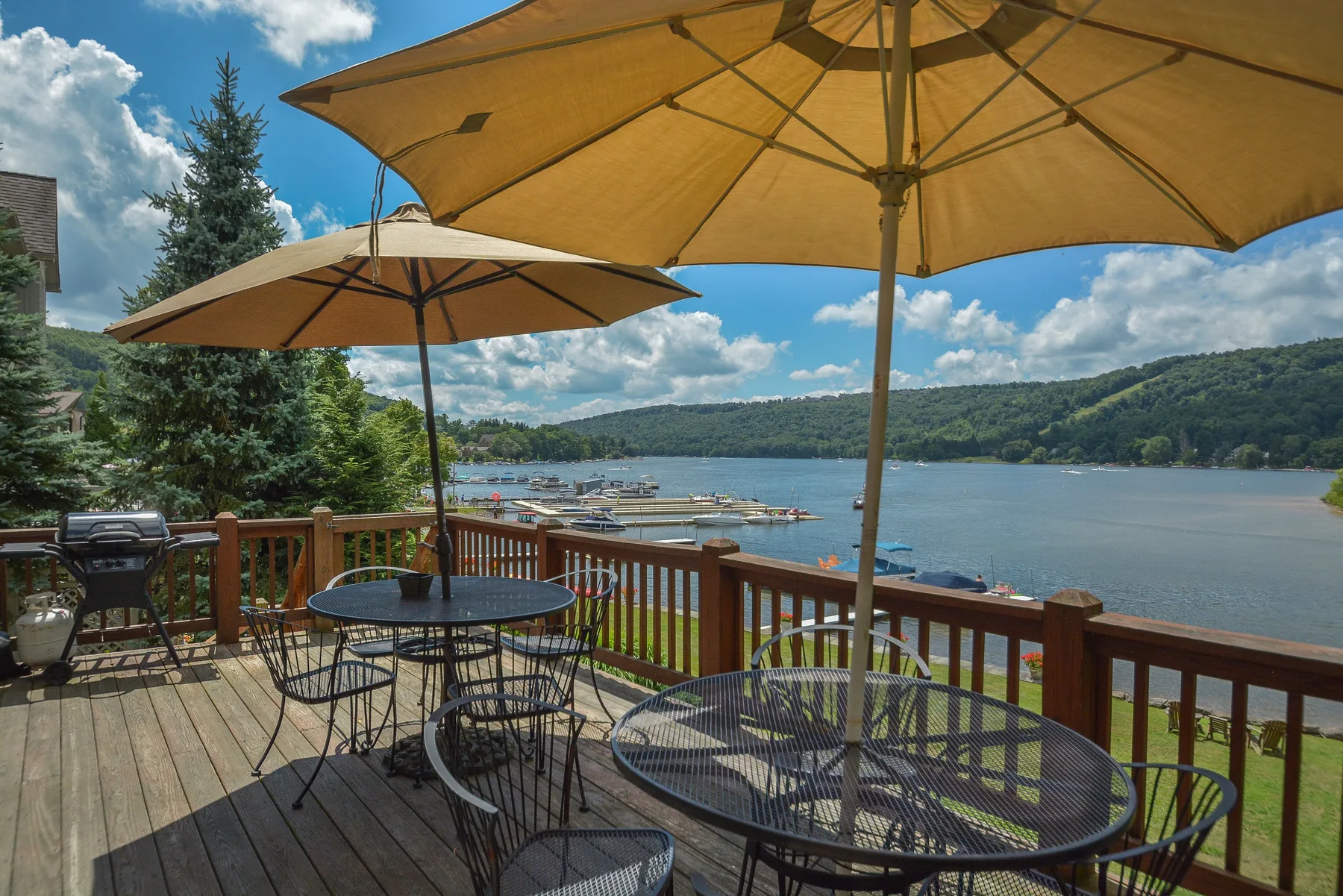 A wooden deck with outdoor seating and umbrellas overlooks a lake.