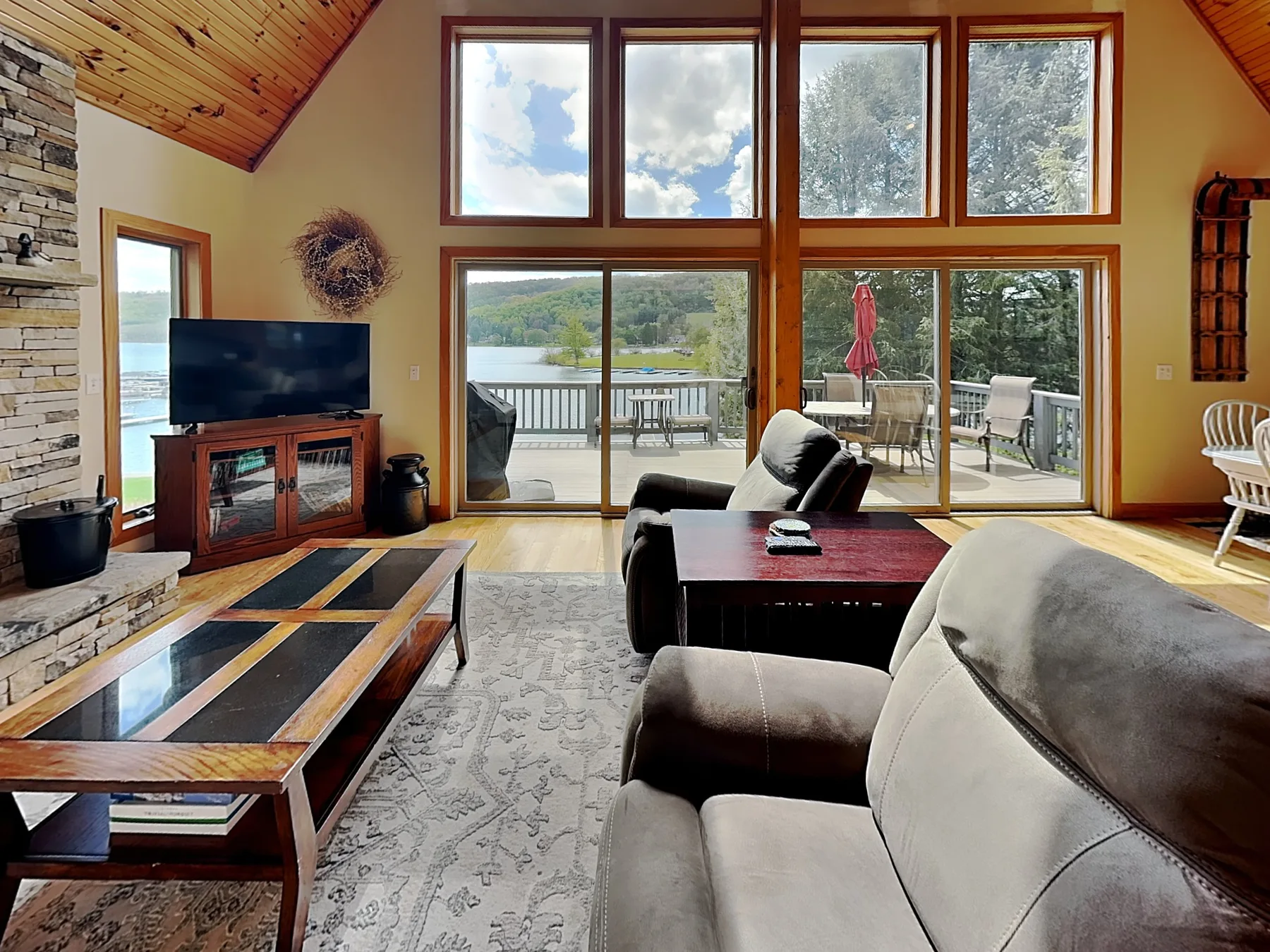 A living room with seating, a television, and large windows overlooking a deck.
