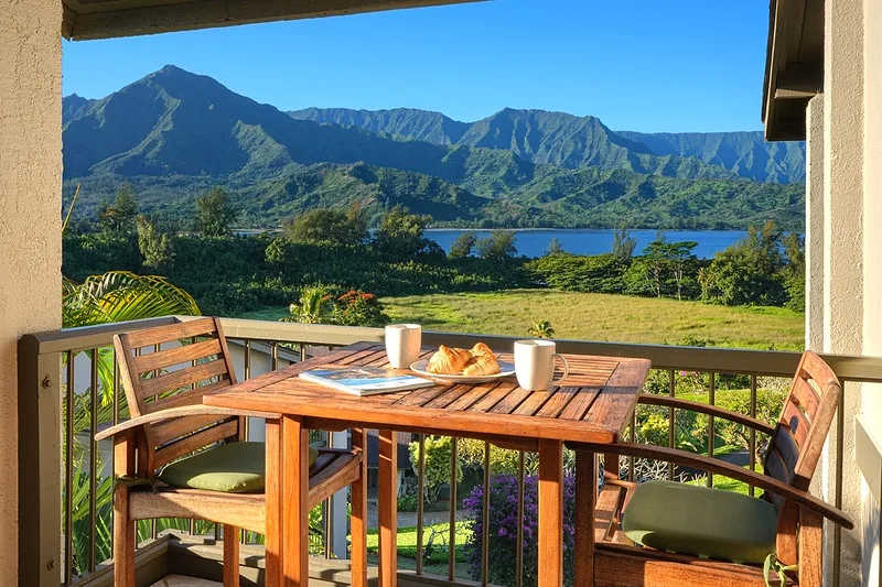A furnished outdoor dining area overlooks a lake and green mountains.