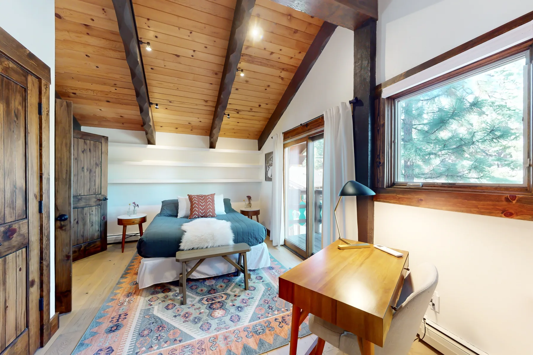 A bedroom with a bed, wooden ceiling beams, and a large window.