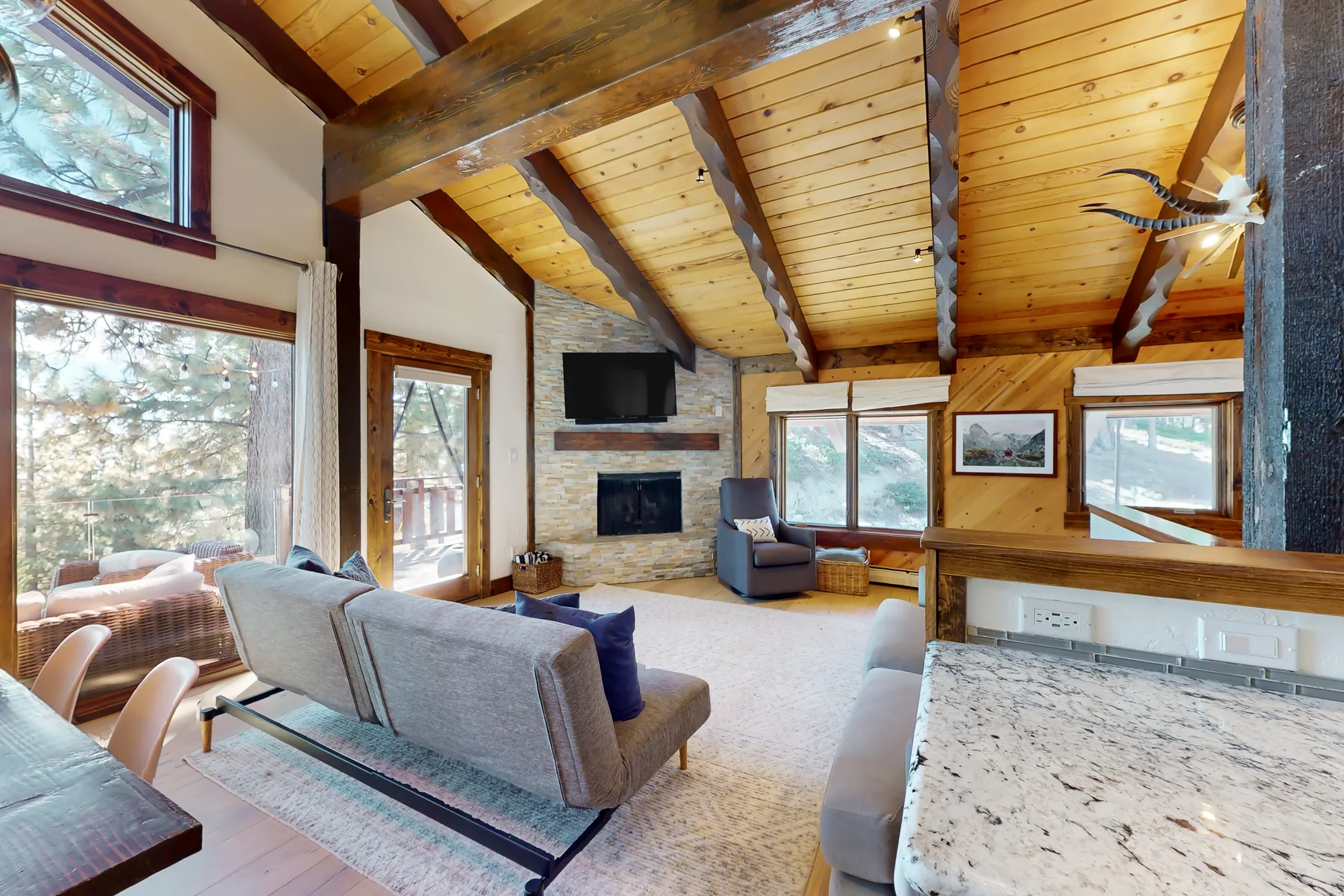 A living room with sloped wood ceilings, large windows, and seating around a fireplace.