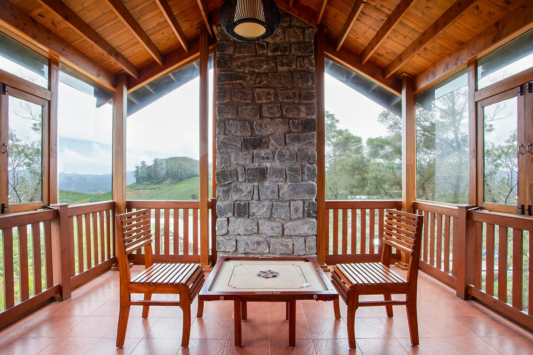 Un porche luminoso y cerrado tiene asientos de madera alrededor de una chimenea de piedra central.