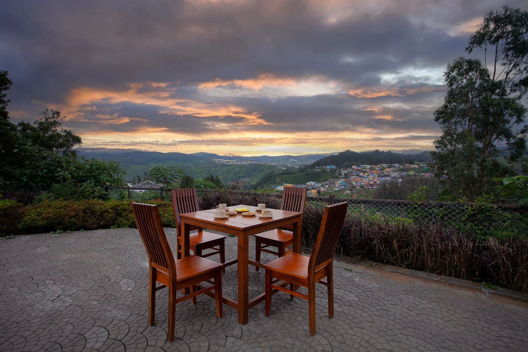 Una zona de comedor al aire libre mira hacia colinas verdes bajo un cielo nublado al atardecer.