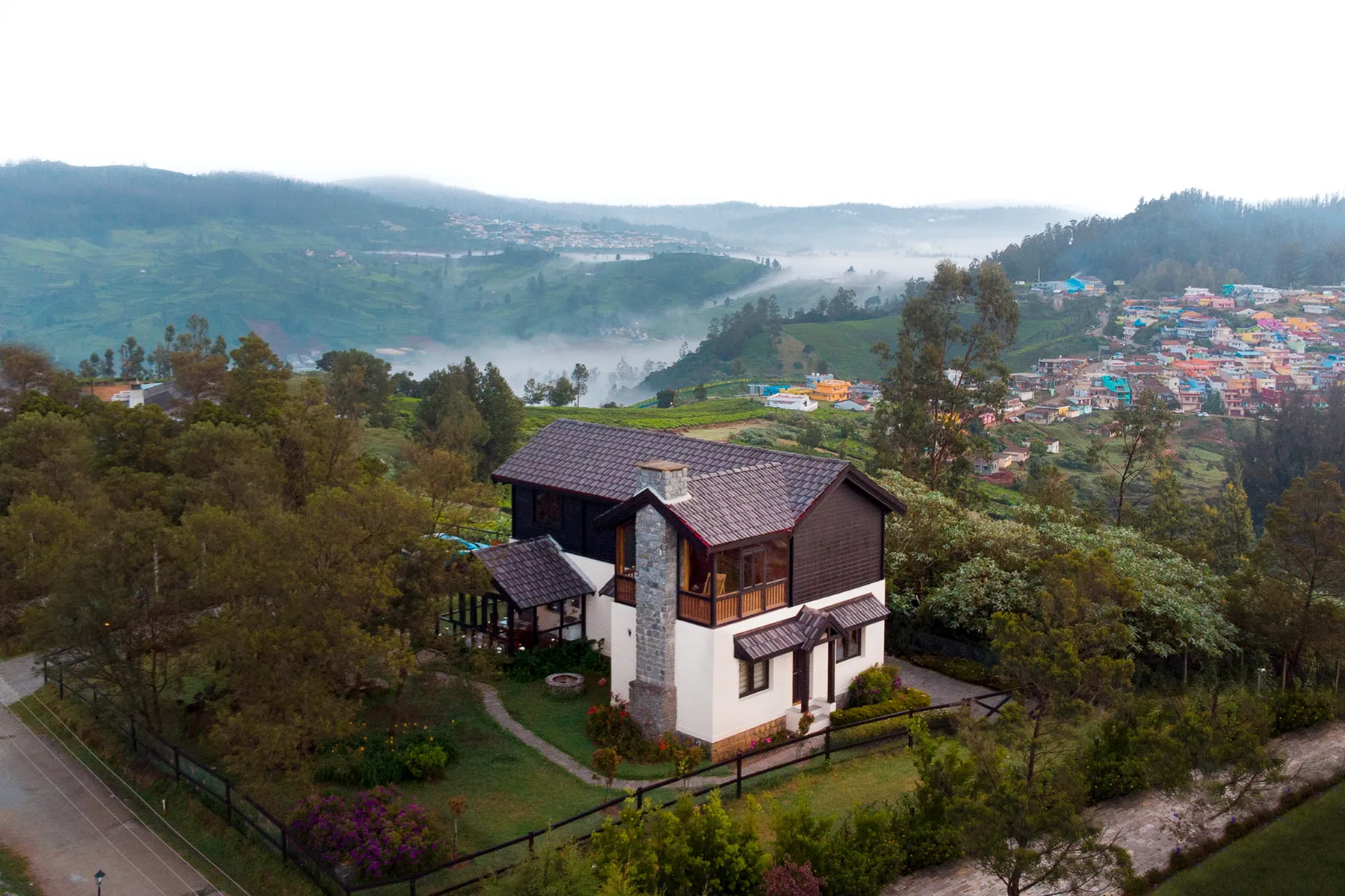 Una casa se encuentra entre árboles en una ladera con vistas a un valle brumoso.