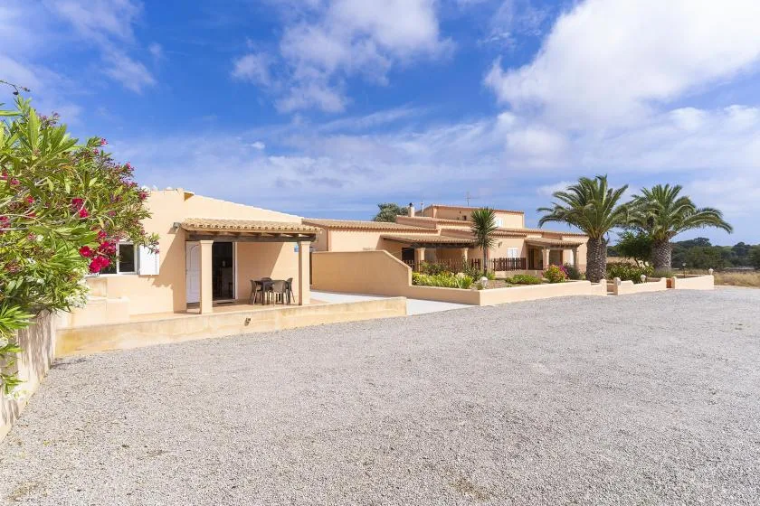 A single-story house with a covered patio faces a broad gravel driveway.