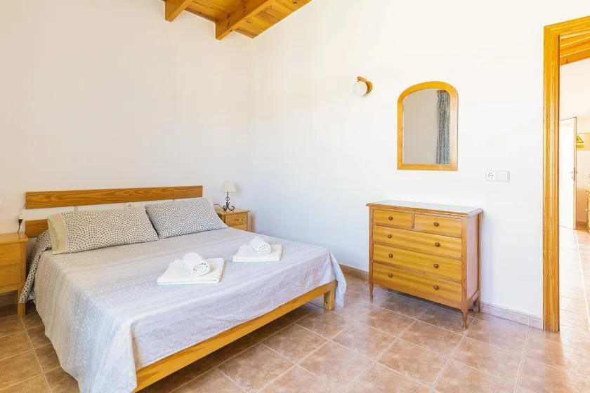 A bedroom with a wooden bed, dresser, and light-colored bedding.