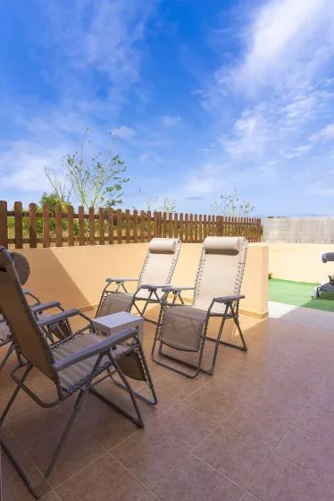 A sunny outdoor patio with reclining seating and a wooden fence.