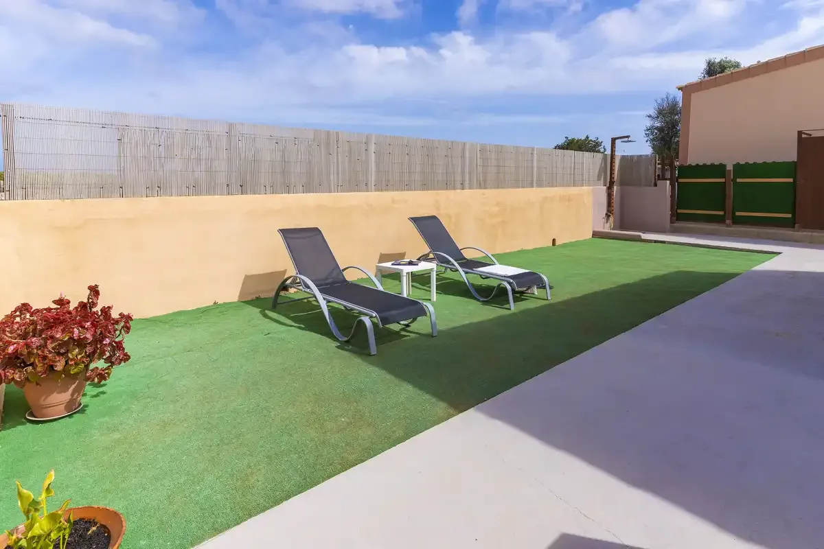 An outdoor patio with lounge seating on artificial grass beside a paved walkway.