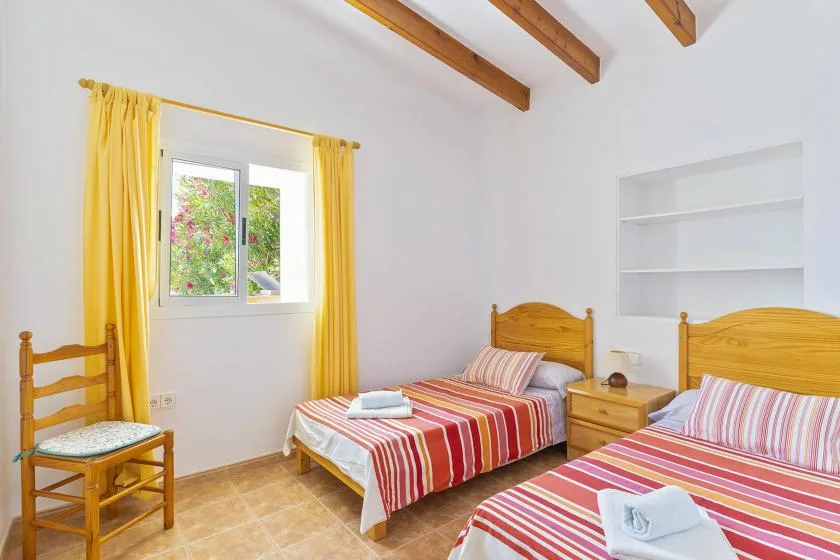A bedroom with two beds dressed in red striped bedding and yellow curtains.