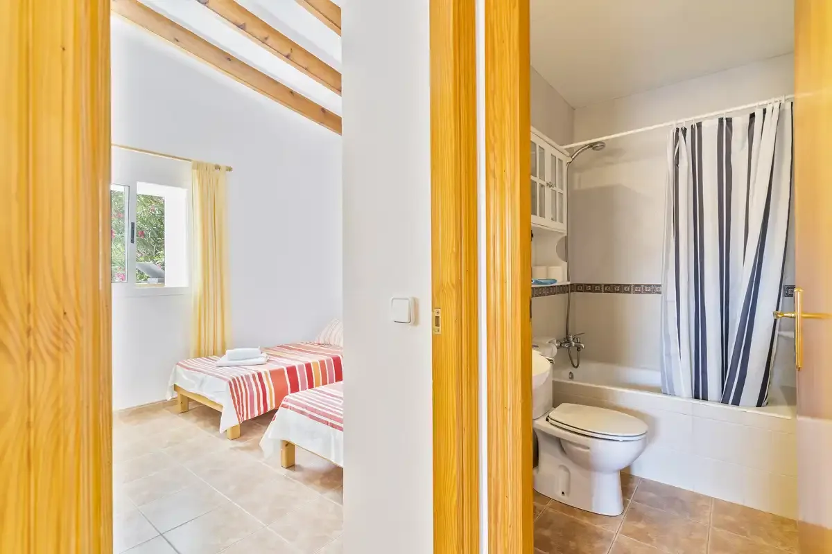 A bedroom with striped bedding is visible beside a bathroom with a shower curtain.