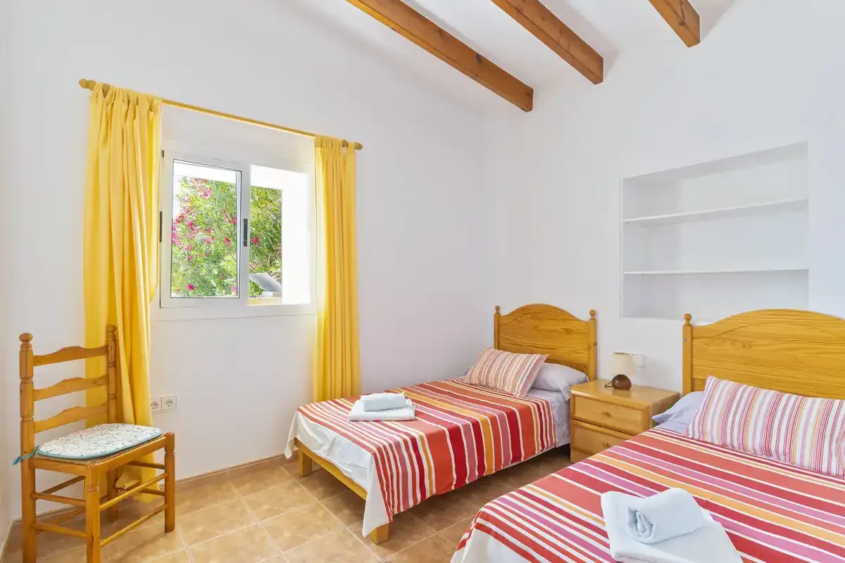 A bright bedroom with two beds, striped bedding, and yellow curtains.