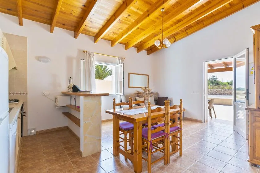 A bright kitchen and dining area with a wooden table beneath exposed ceiling beams.
