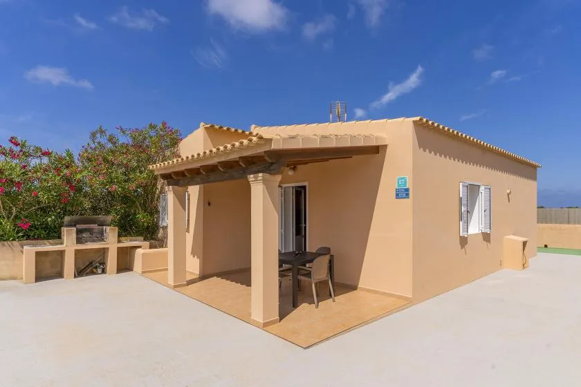 A small house with a covered patio and outdoor seating under a clear blue sky.