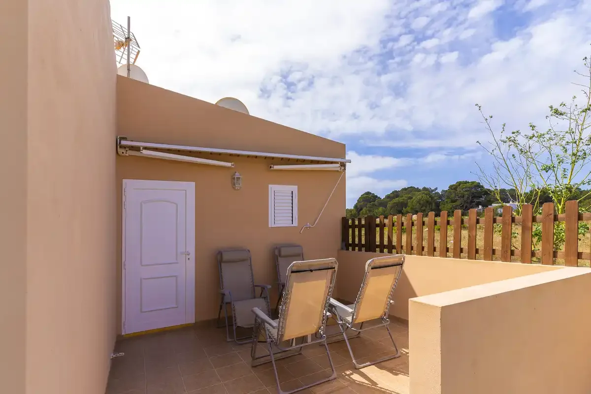 A sunny outdoor terrace with reclining seating beside a peach-colored building.