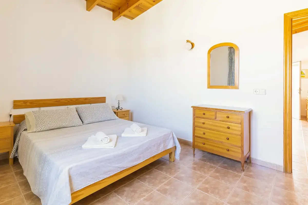 A bedroom with a wooden bed, dresser, and a doorway to the adjoining space.
