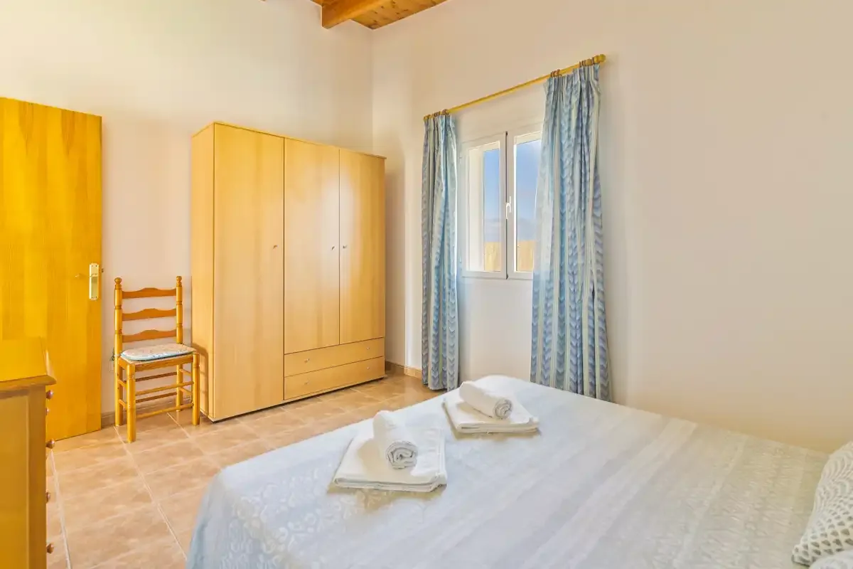 A bedroom with a bed, wooden wardrobes, and a window with blue curtains.