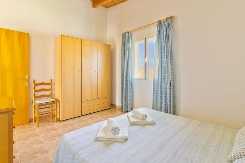 A bedroom with a bed, wardrobe, and window with blue curtains.