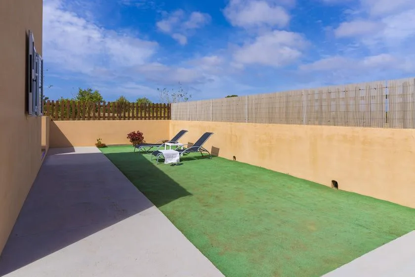 Outdoor patio with a green lawn and two loungers beside a low wall.
