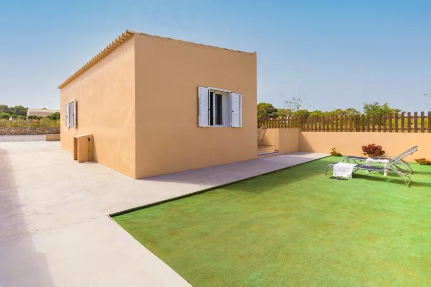 A small stucco building beside a paved patio and green lawn.
