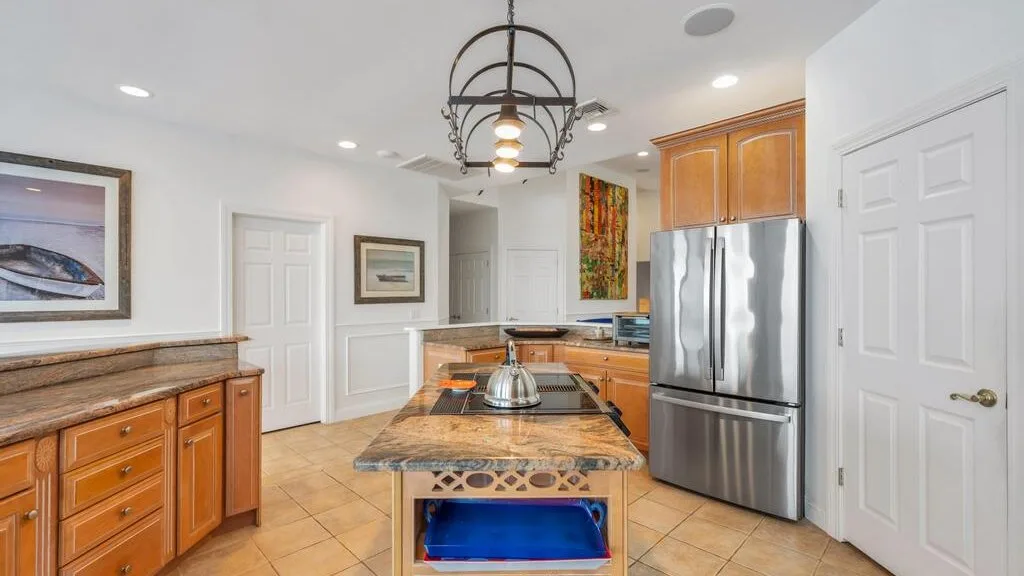 A bright kitchen with a central island, wooden cabinets, and a stainless steel refrigerator.
