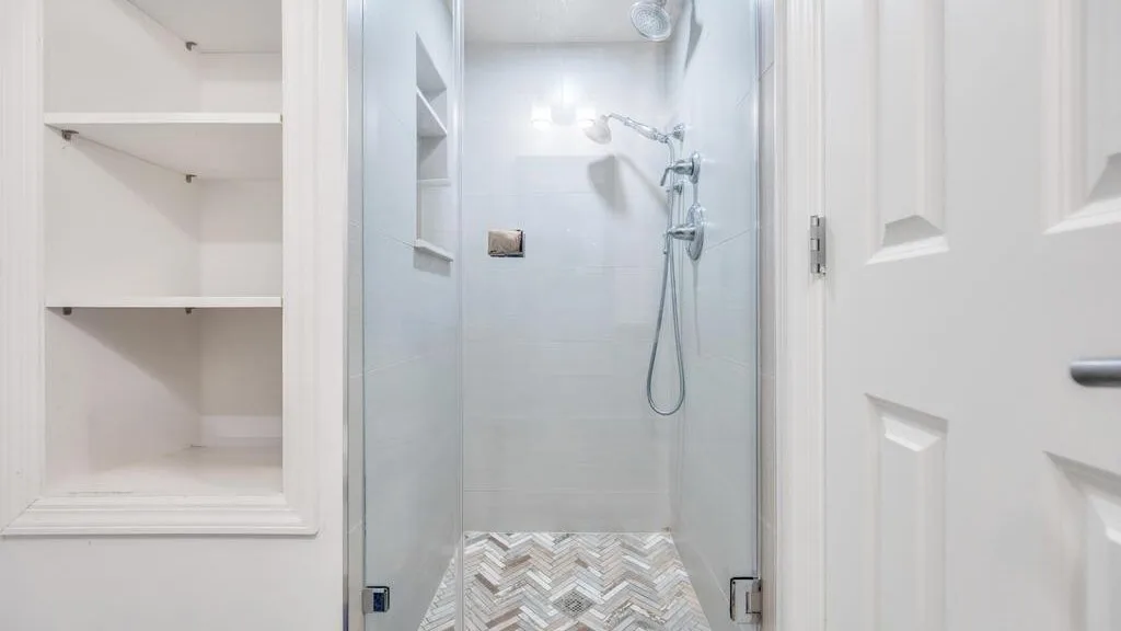 A bright bathroom shower with recessed wall shelves and patterned floor tiles.