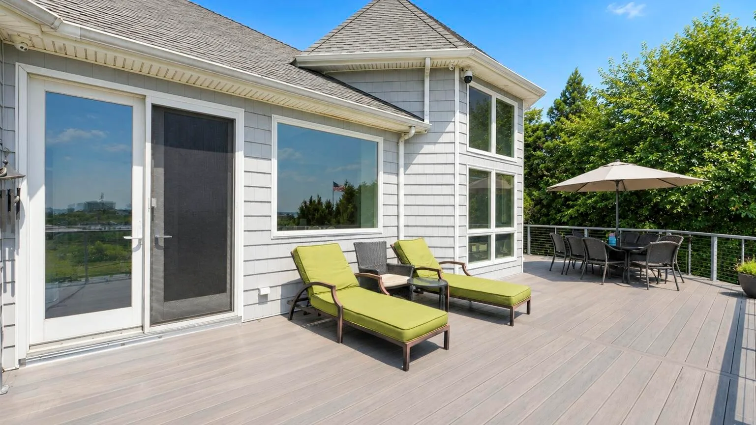 A spacious outdoor deck with lounge seating and a dining table beneath an umbrella.