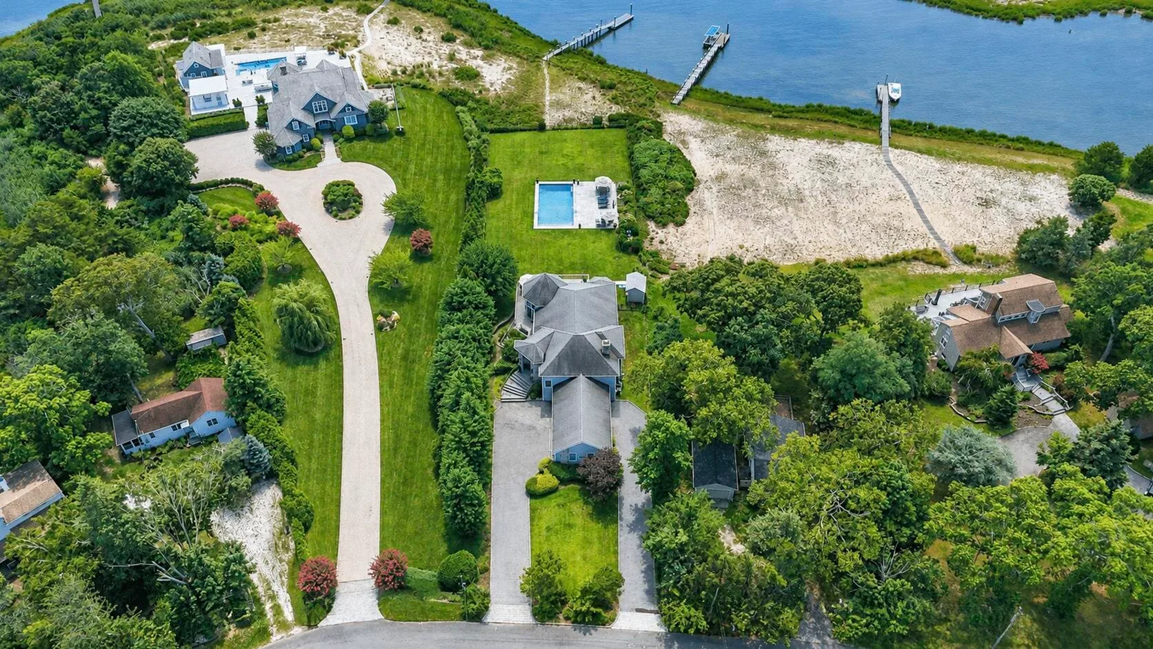 Aerial view of a landscaped property beside a waterway, with a pool and dock.