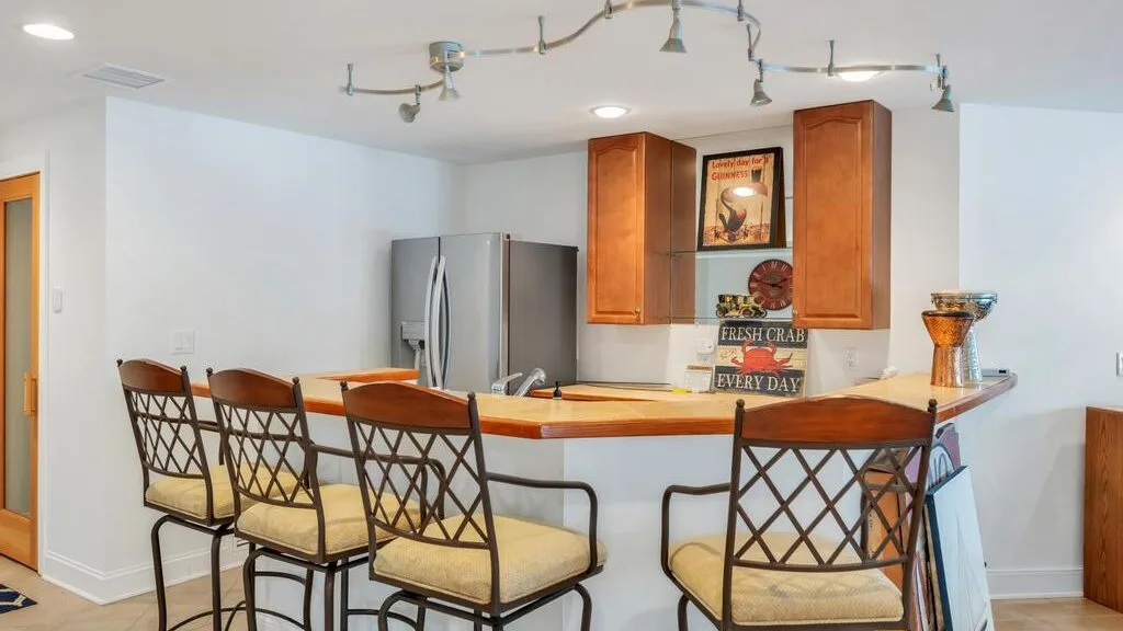 A kitchen bar with several stools, wooden cabinets, and a refrigerator.