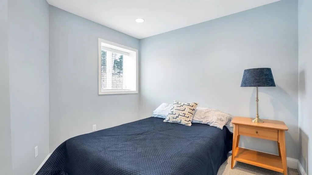 A bedroom with a bed, pillows, and a bedside table beneath a lamp.