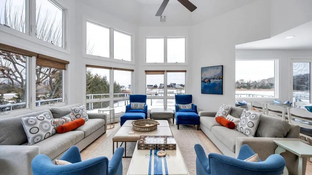 A bright living room with large windows and blue seating around a central table.