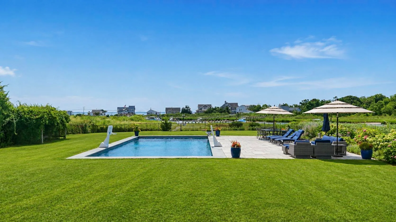 An outdoor swimming pool sits beside a lawn and shaded seating area.