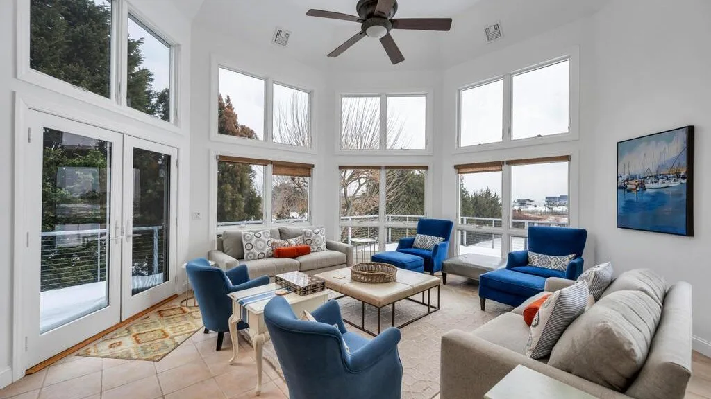 A bright living room with large windows and seating around a coffee table.