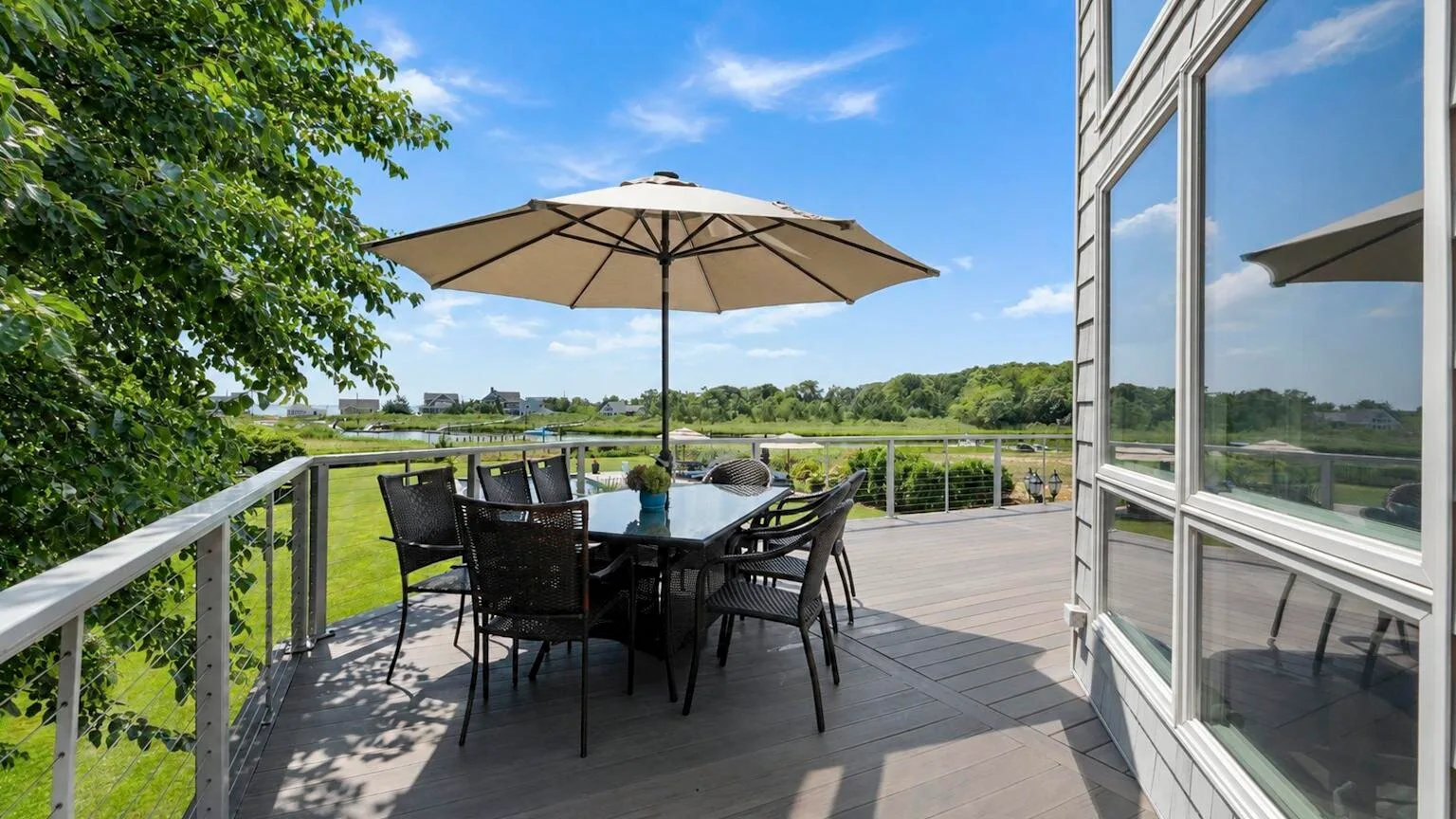 An outdoor deck with seating beneath a large umbrella overlooks green fields.