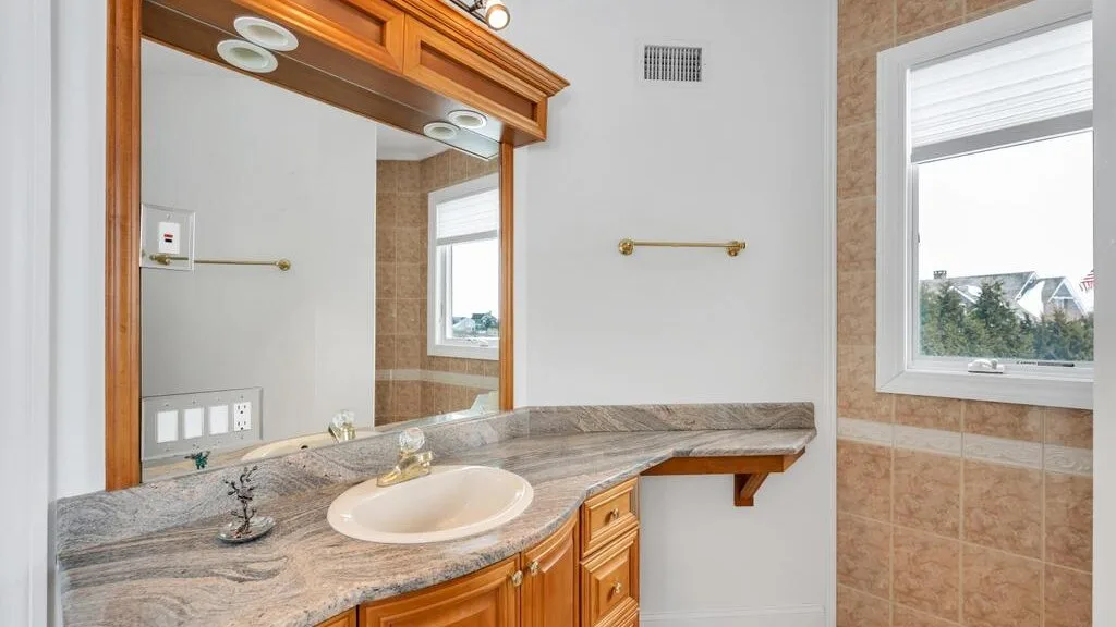 A bathroom vanity with a large mirror, stone countertop, and sink.