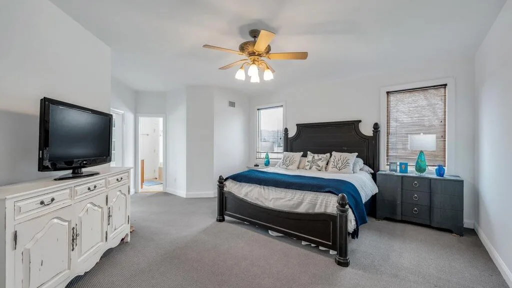 A bedroom with a dark bed, white dresser, and television.