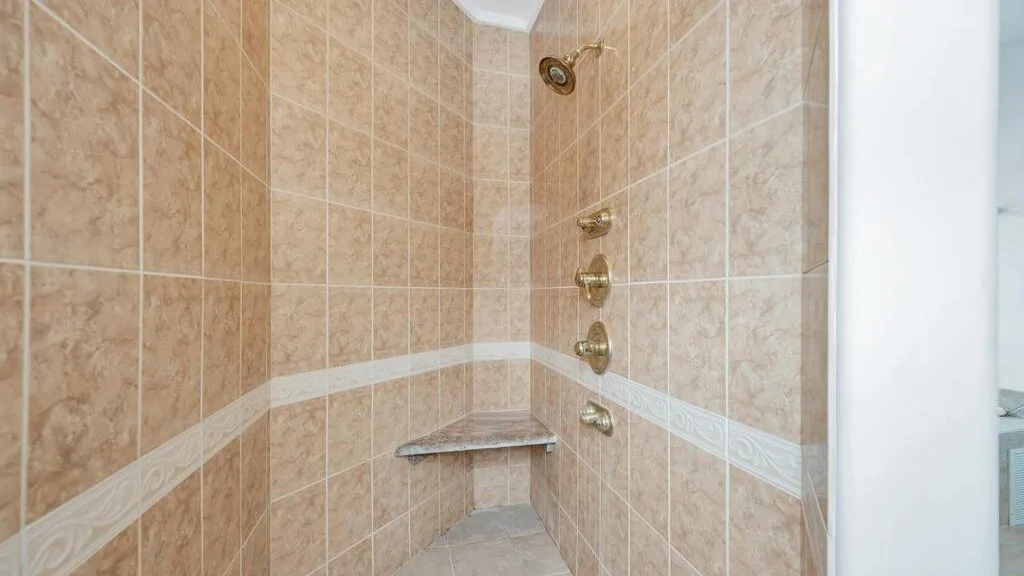 A tiled shower with wall-mounted fixtures and a small corner shelf.