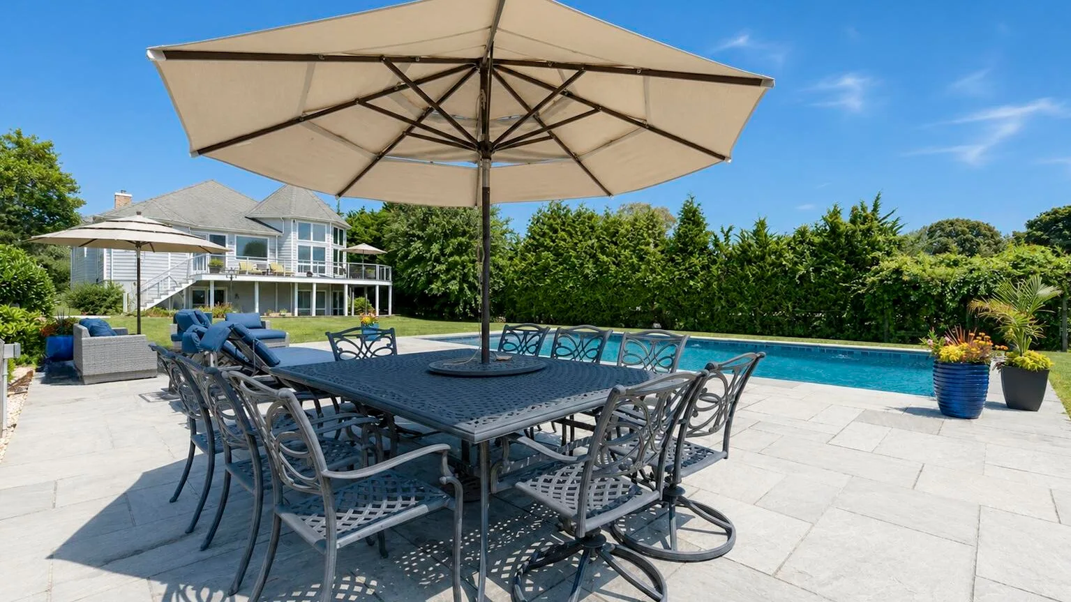 An outdoor dining area beside a swimming pool, shaded by a large umbrella.