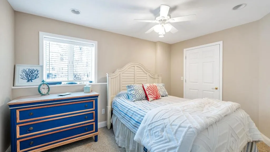 A bedroom with a bed, blue dresser, and window with blinds.