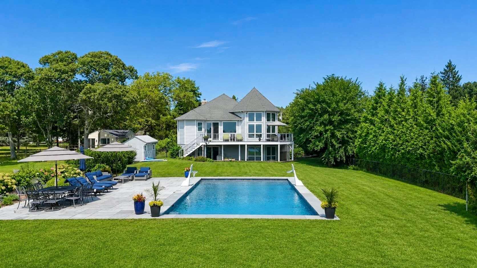 A large house overlooks a backyard pool, patio seating, and a broad green lawn.