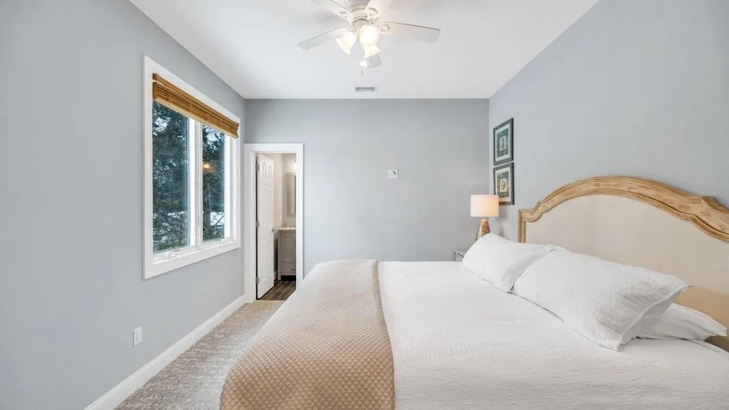 A bright bedroom with a large bed and a window overlooking trees.