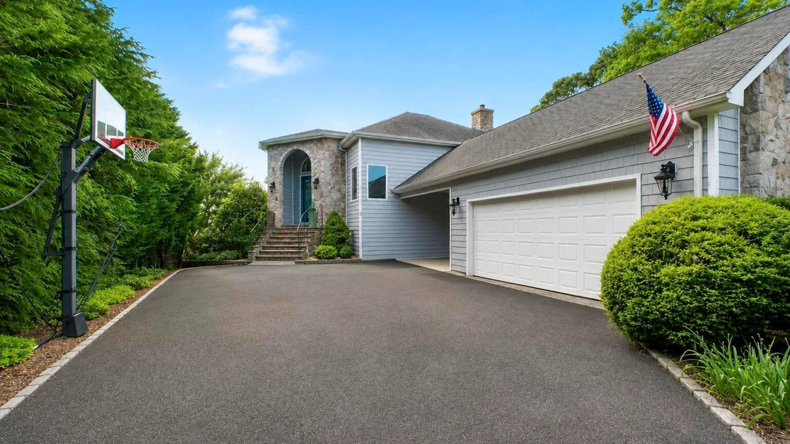 A paved driveway leads to a house with a garage and basketball hoop.