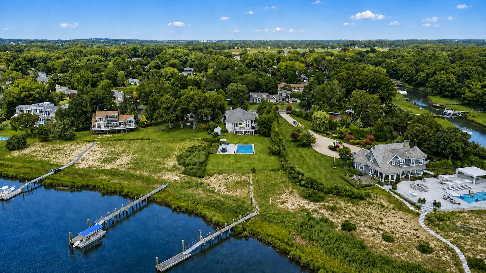 Aerial view of waterfront homes along a tree-lined river, with docks and a pool.