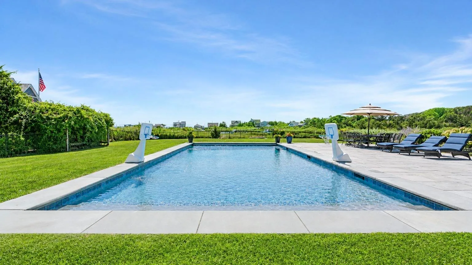 An outdoor swimming pool is bordered by lounge seating and green lawns.
