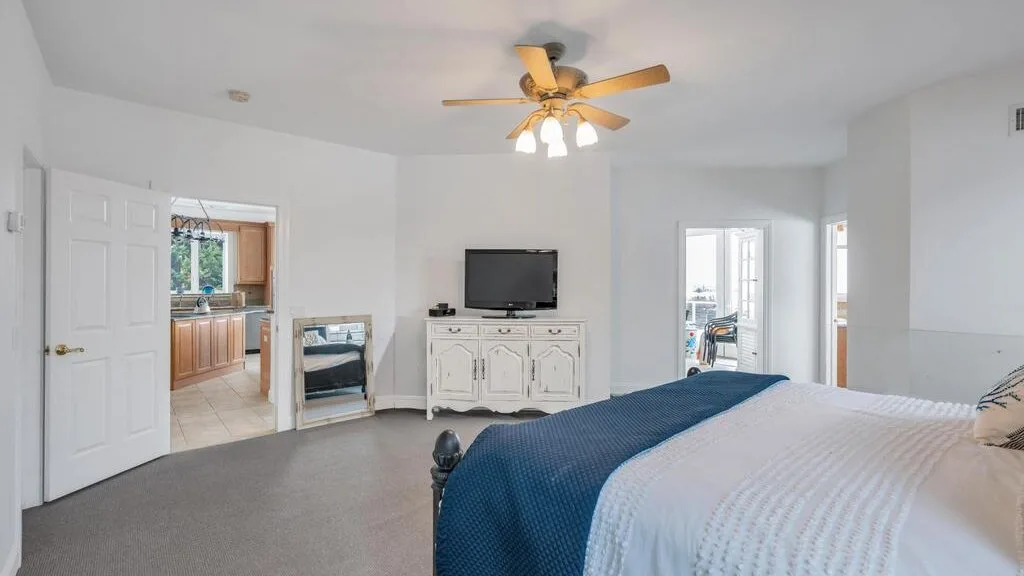 A bedroom with a bed, a television on a cabinet, and a ceiling fan.