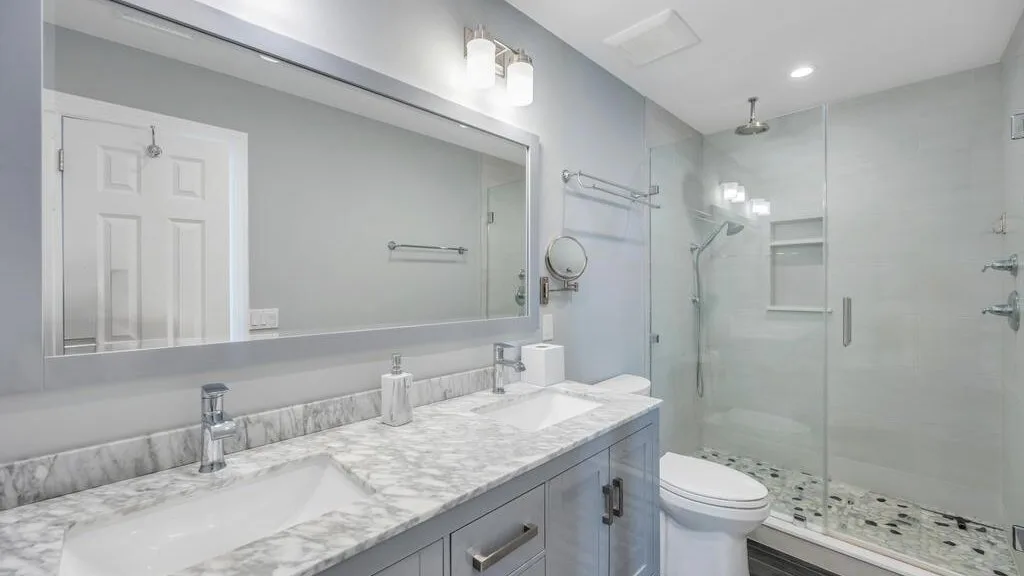 A bright bathroom with a long vanity, a toilet, and a glass shower.