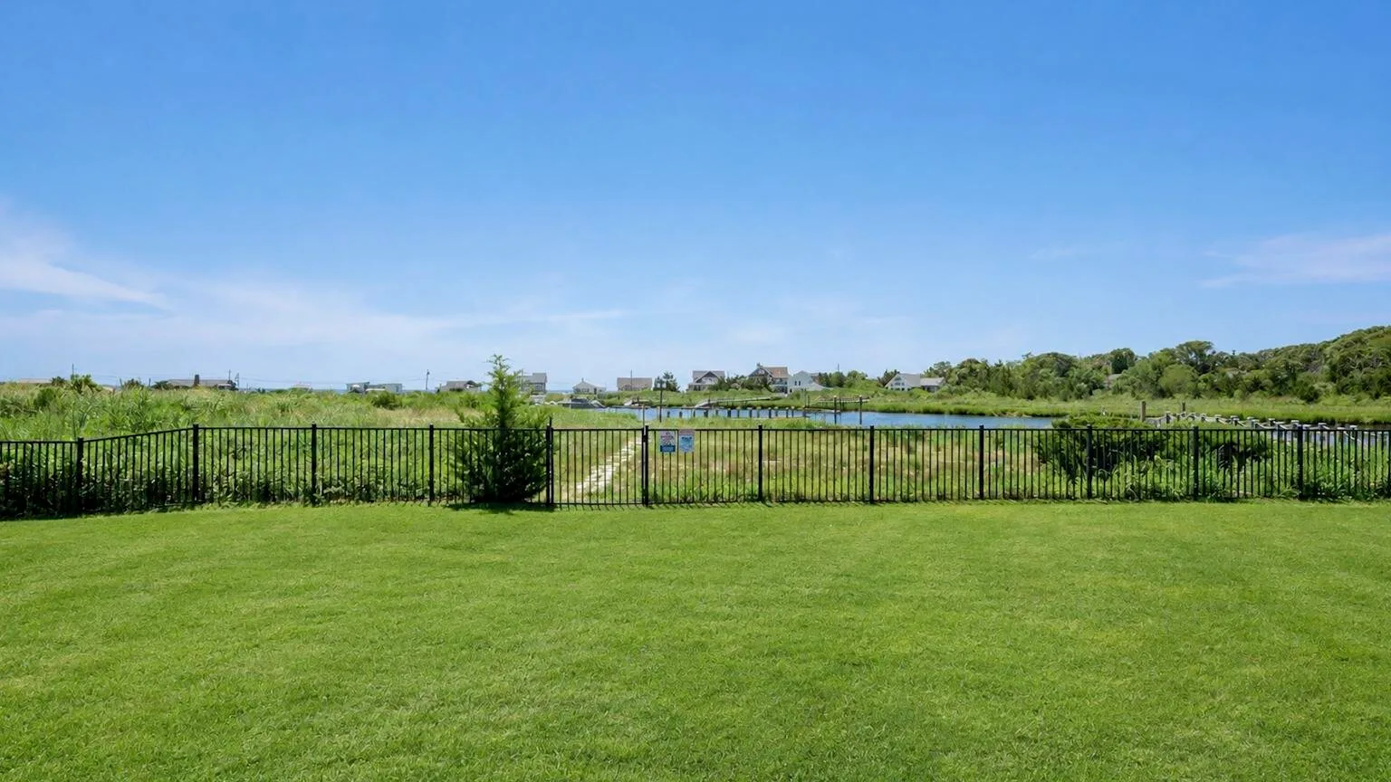 A broad green lawn stretches toward a black fence and open fields.