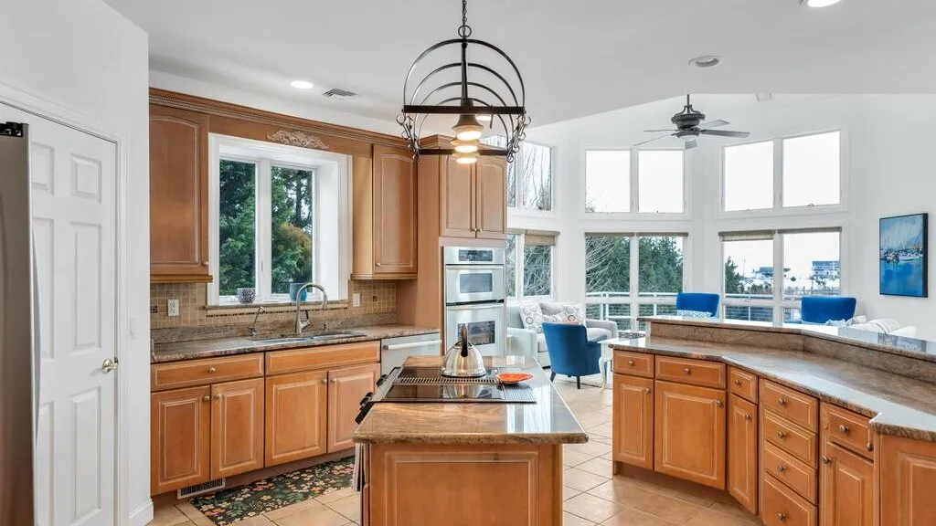 A bright kitchen with wooden cabinets, a central island, and large windows.