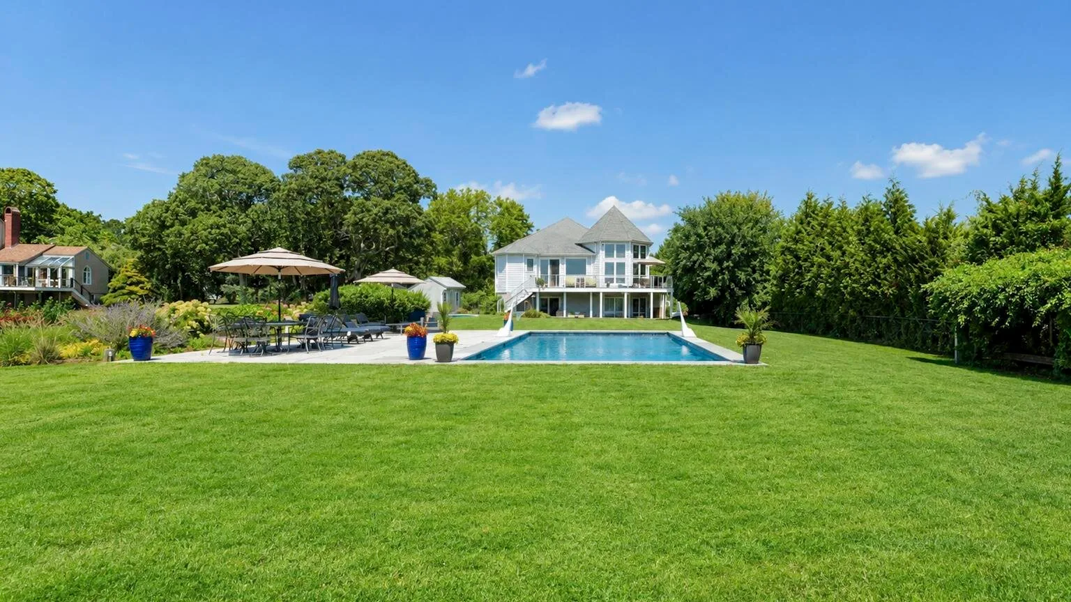 A large green lawn leads to a swimming pool and a white house.