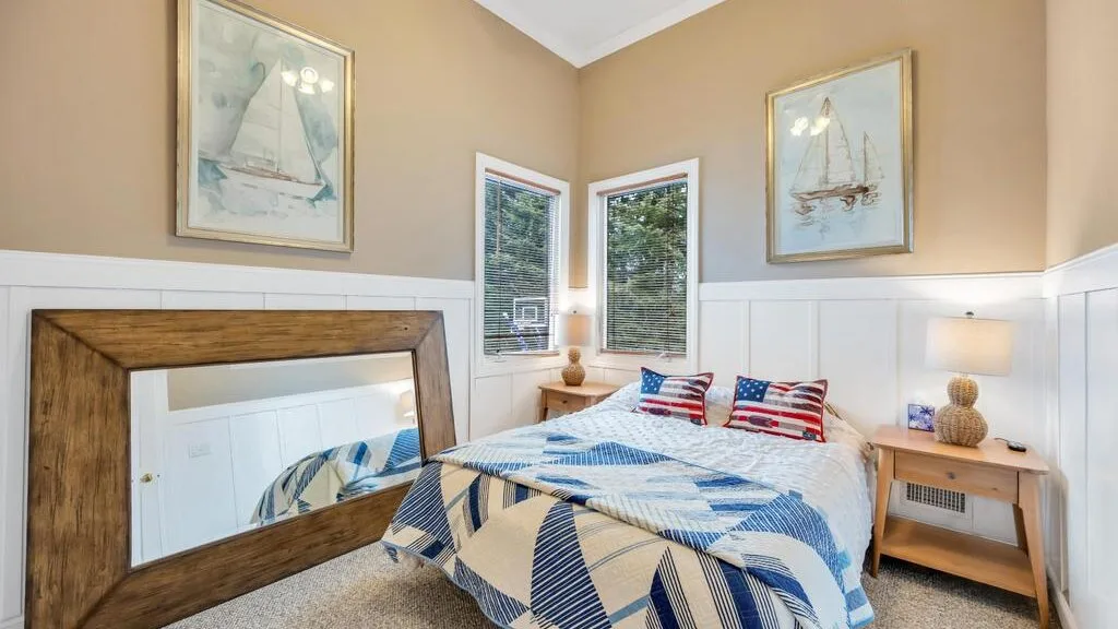 A bedroom with a bed dressed in blue-and-white bedding and framed sailboat art.